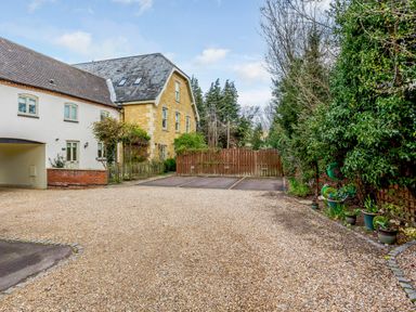 A gravel driveway with parking spaces next to a two-story house surrounded by trees at Jasmine Cottage in Mickleton Gloucestershire