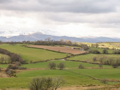 A rural landscape with green and brown fields trees and snow covered mountains in the background at Orsedd Wen Farmhouse in Betws-Y-Coed