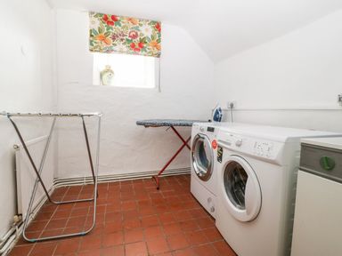 A laundry room with a washing machine dryer ironing board and drying rack at Orsedd Wen Farmhouse in Betws-Y-Coed