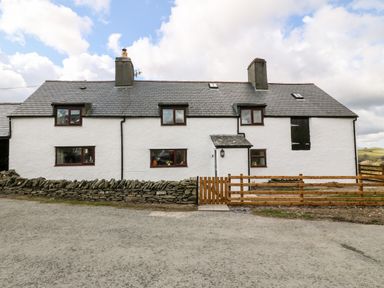 A white farmhouse with a slate roof a stone wall and a wooden gate at Orsedd Wen Farmhouse in Betws-Y-Coed