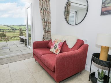 A living room with a red sofa and a view of the outdoors at Orsedd Wen Farmhouse in Betws-Y-Coed