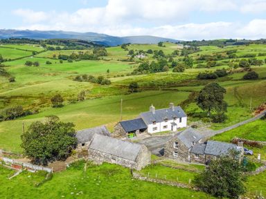 An aerial view of a farmhouse surrounded by fields and trees at Orsedd Wen Farmhouse in Betws-Y-Coed