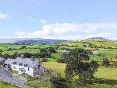 A house in a field with mountains in the background at Orsedd Wen Farmhouse Betws-Y-Coed