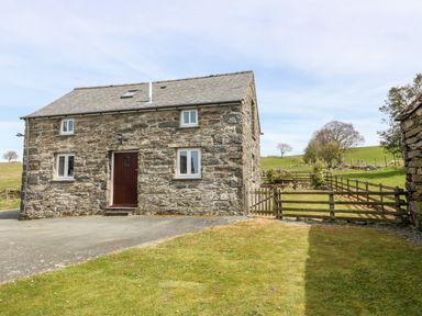 A stone cottage with a dark wooden door and white framed windows with a wooden fence and green field in the background at Orsedd Wen Cottage in Betws-Y-Coed