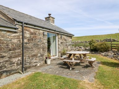 A stone cottage with a wooden picnic table on a stone patio in a grassy yard at Orsedd Wen Cottage in Betws-Y-Coed