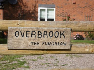 A wooden sign with the text Overbrook The Fungalow on a wooden fence with a brick house in the background at Overbrook in Salwarpe near Droitwich Spa
