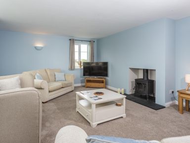 A living room with beige sofas a white coffee table a television and a black wood stove at Overbrook in Salwarpe near Droitwich Spa