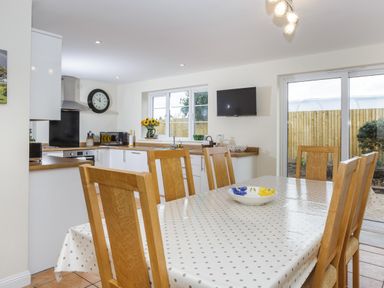 A kitchen and dining area with wooden chairs around a table covered with a polka dot tablecloth and a sliding glass door at Overbrook in Salwarpe near Droitwich Spa