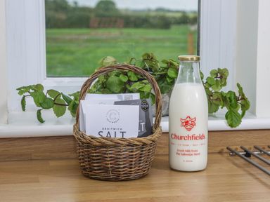 A wicker basket with salt packets and a bottle of milk on a kitchen counter by a window with a plant at Overbrook in Salwarpe near Droitwich Spa