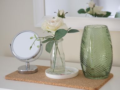 A table with a round mirror white flowers in a glass bottle and a green textured vase at Overbrook in Salwarpe near Droitwich Spa