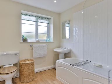 A bathroom with a toilet a wicker laundry basket a towel rack a sink a bathtub with a glass screen and tiled walls at Overbrook in Salwarpe near Droitwich Spa