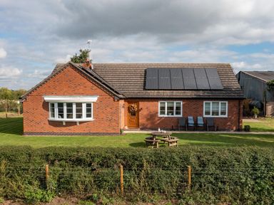 A brick house with solar panels on the roof lawn picnic table and chairs at Overbrook in Salwarpe near Droitwich Spa