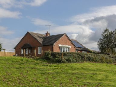 A brick house with solar panels on the roof behind a fenced grassy field at Overbrook in Salwarpe near Droitwich Spa
