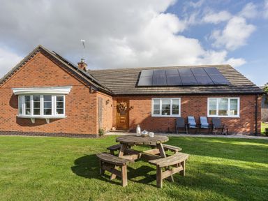 A brick house with solar panels on the roof a wooden picnic table on the lawn and chairs near the windows at Overbrook in Salwarpe near Droitwich Spa