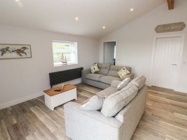 A living room with two grey sofas a wooden coffee table a model sailboat on a window sill and a framed turtle picture on the wall at Caban Y Mor in Amroth near Saundersfoot