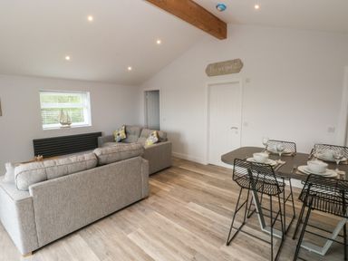 A living room with two gray sofas and a dining table set for four at Caban Y Mor in Amroth near Saundersfoot