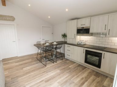 A kitchen with a dining table set for four and modern appliances at Caban Y Mor in Amroth near Saundersfoot