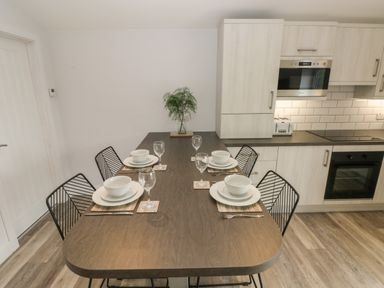 A dining table set with plates bowls glasses and cutlery in a kitchen with cabinets and appliances at Caban Y Mor in Amroth near Saundersfoot