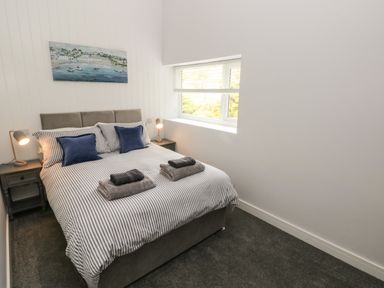 A bedroom with a bed flanked by two bedside tables and lamps and a window to the right at Caban Y Mor in Amroth near Saundersfoot