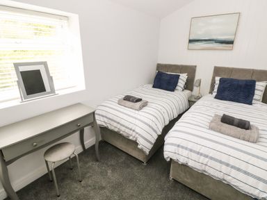 A bedroom with two single beds a desk with a stool and a mirror on the windowsill at Caban Y Mor in Amroth near Saundersfoot