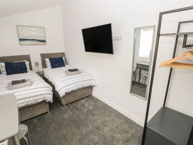 A bedroom with two single beds a wall-mounted TV a full-length mirror and an open wardrobe at Caban Y Mor in Amroth near Saundersfoot