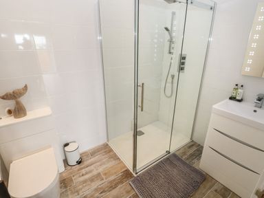 A bathroom with a toilet a glass shower enclosure a sink with drawers and a grey bath mat on the floor at Caban Y Mor in Amroth near Saundersfoot