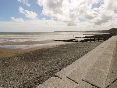 A pebble and sand beach with wooden groynes and a concrete sea wall under a cloudy sky at Caban Y Mor in Amroth near Saundersfoot