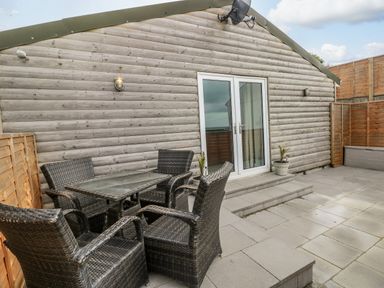 An outdoor patio area with a glass table and four wicker chairs in front of a wooden building at Caban Y Mor in Amroth near Saundersfoot