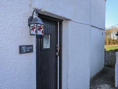 A black wooden door with a decorative stained glass lantern and a sign that reads Oscars Pad on a textured white wall at Oscars Pad in Brynsiencyn