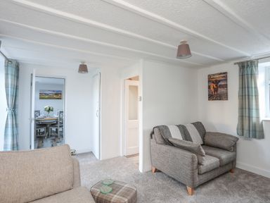A living room with two armchairs and a small ottoman with curtains on windows and a painting on the wall at Oscars Pad in Brynsiencyn