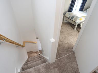 A carpeted staircase with wooden handrail next to a bedroom with a bed and window at Oscars Pad in Brynsiencyn