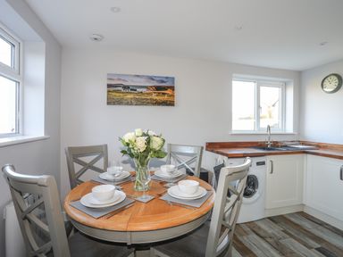 A kitchen with a round dining table set with plates bowls wine glasses and a vase of flowers at Oscars Pad in Brynsiencyn