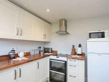 A kitchen with white cabinets wooden countertops a stove a microwave on a refrigerator and kitchen utensils at Oscars Pad in Brynsiencyn