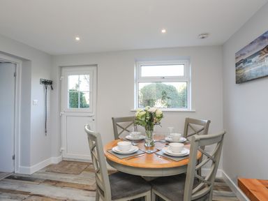 A dining area with a round wooden table set for four and a door and window in the background at Oscars Pad in Brynsiencyn