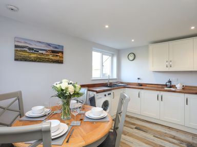 A kitchen with wooden table set for four with white dishes and a vase of flowers white cabinets and wood countertops at Oscars Pad in Brynsiencyn