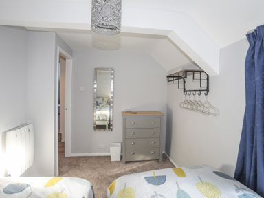 A bedroom with two beds a dresser a wall mirror hangers on a rack and blue curtains at Oscars Pad in Brynsiencyn
