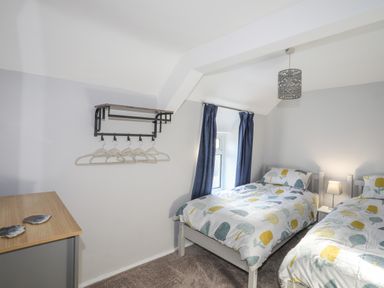 A bedroom with two single beds a wooden table and a wall-mounted clothes rack at Oscars Pad in Brynsiencyn