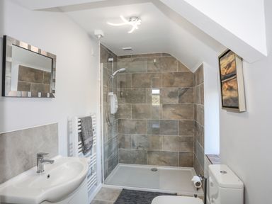 A bathroom with a shower area tiled with brown tiles a white sink mirror radiator with towel and a toilet at Oscars Pad in Brynsiencyn
