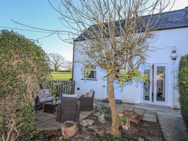 An outdoor patio area with garden furniture and a tree next to a white house at Oscars Pad in Brynsiencyn