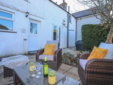 A patio with wicker chairs and a table with wine glasses and a bottle at Oscars Pad in Brynsiencyn