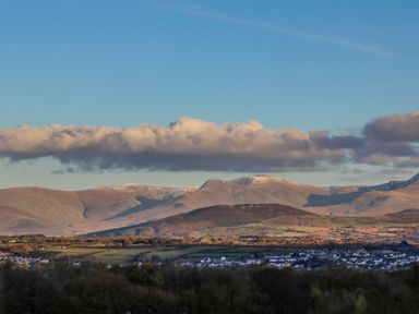 A landscape of mountains with a small village and trees under a blue sky with clouds at Oscars Pad in Brynsiencyn