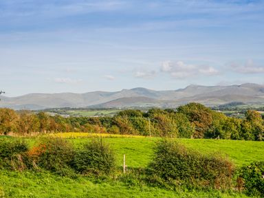 A rural landscape with green fields trees and distant mountains at Oscars Pad in Brynsiencyn