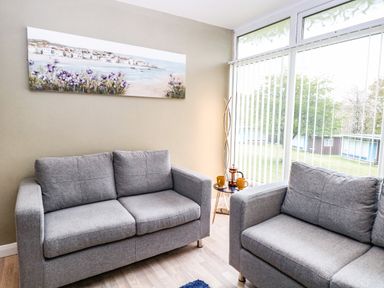 A sitting area with two grey sofas and a small round table with cups and a teapot by a window at Chalet 126a in Cromer