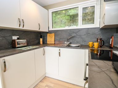 A kitchen with white cabinets gray countertops a window and various appliances at Chalet 126a in Cromer