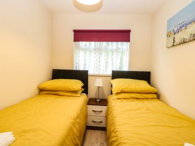 A bedroom with two single beds with yellow bedding and a small bedside table with a lamp at Chalet 126a in Cromer