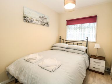 A bedroom with a bed neatly made with folded towels on it next to a nightstand with a lamp and a window with a red blind at Chalet 126a in Cromer