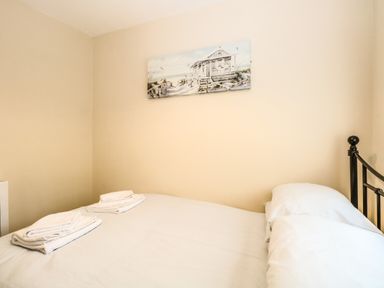 A bedroom with a bed made with white linens and towels on it and a beach house painting on the wall at Chalet 126a in Cromer