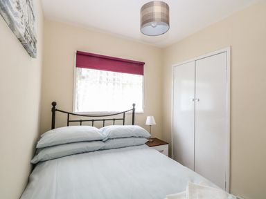 A bedroom with a double bed stacked with pillows beside a window with a purple blind and a white built in closet at Chalet 126a Cromer