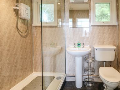 A bathroom with a shower enclosure a pedestal sink a toilet and two frosted windows at Chalet 126a in Cromer