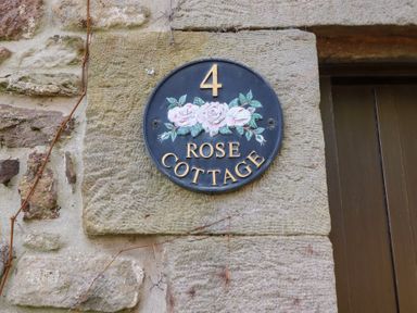 A round sign with the number 4 and text Rose Cottage mounted on a stone wall at Rose Cottage Akeld near Wooler